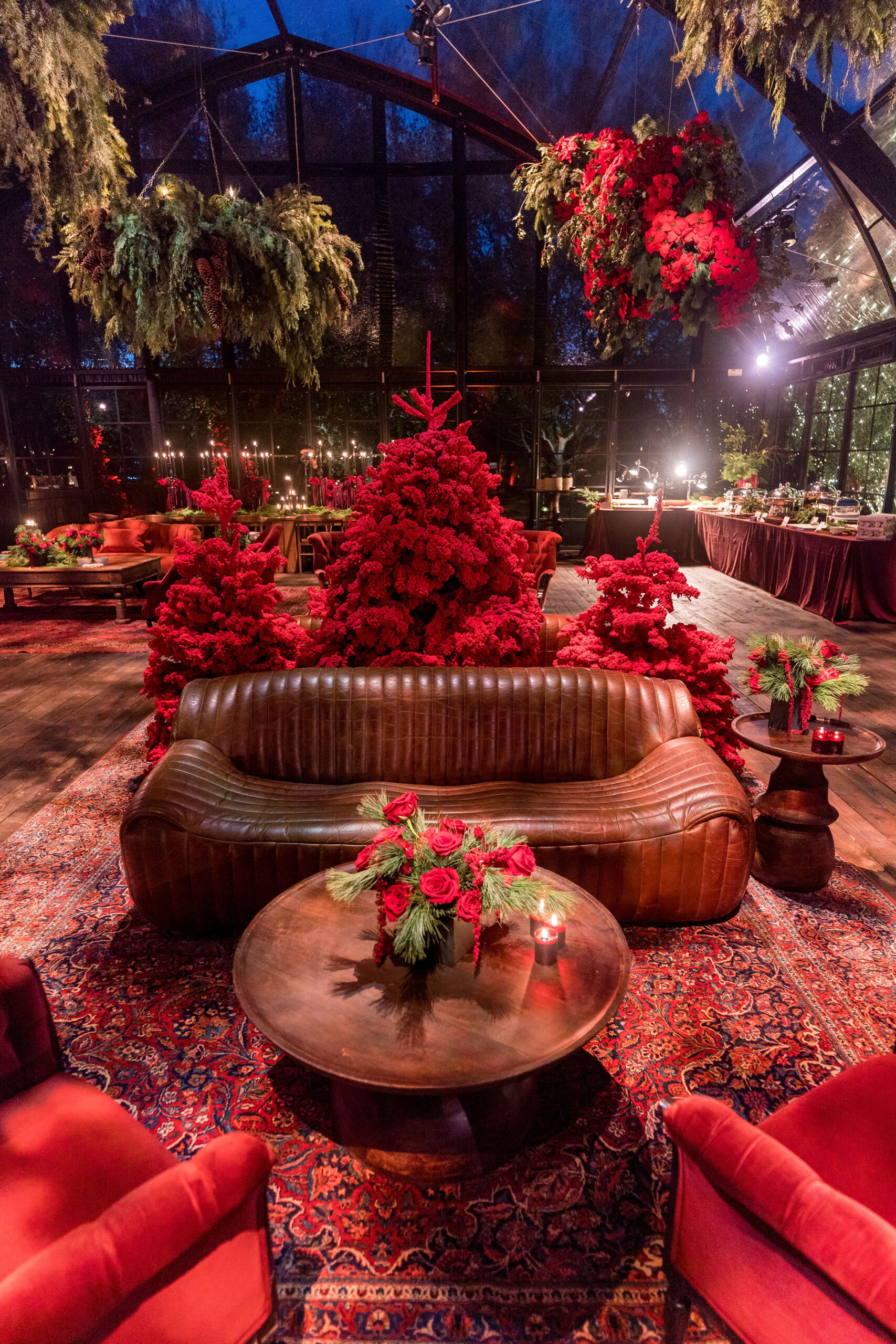 Front view of modern cognac leather tufted sofa on vintage Persian rugs surrounded by ferns and poinsettia in a glass tent at Kourtney Kardashian Barker&#8217;s 2022 Christmas Eve party