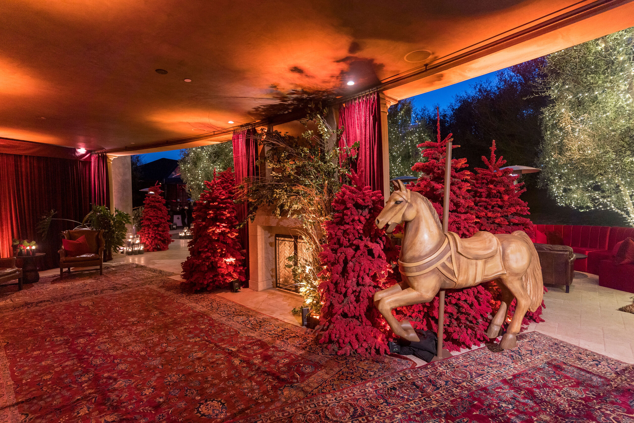 Kourtney Kardashian Barker&#8217;s Christmas eve party 2022 vintage carousel horse in front of red trees at the window