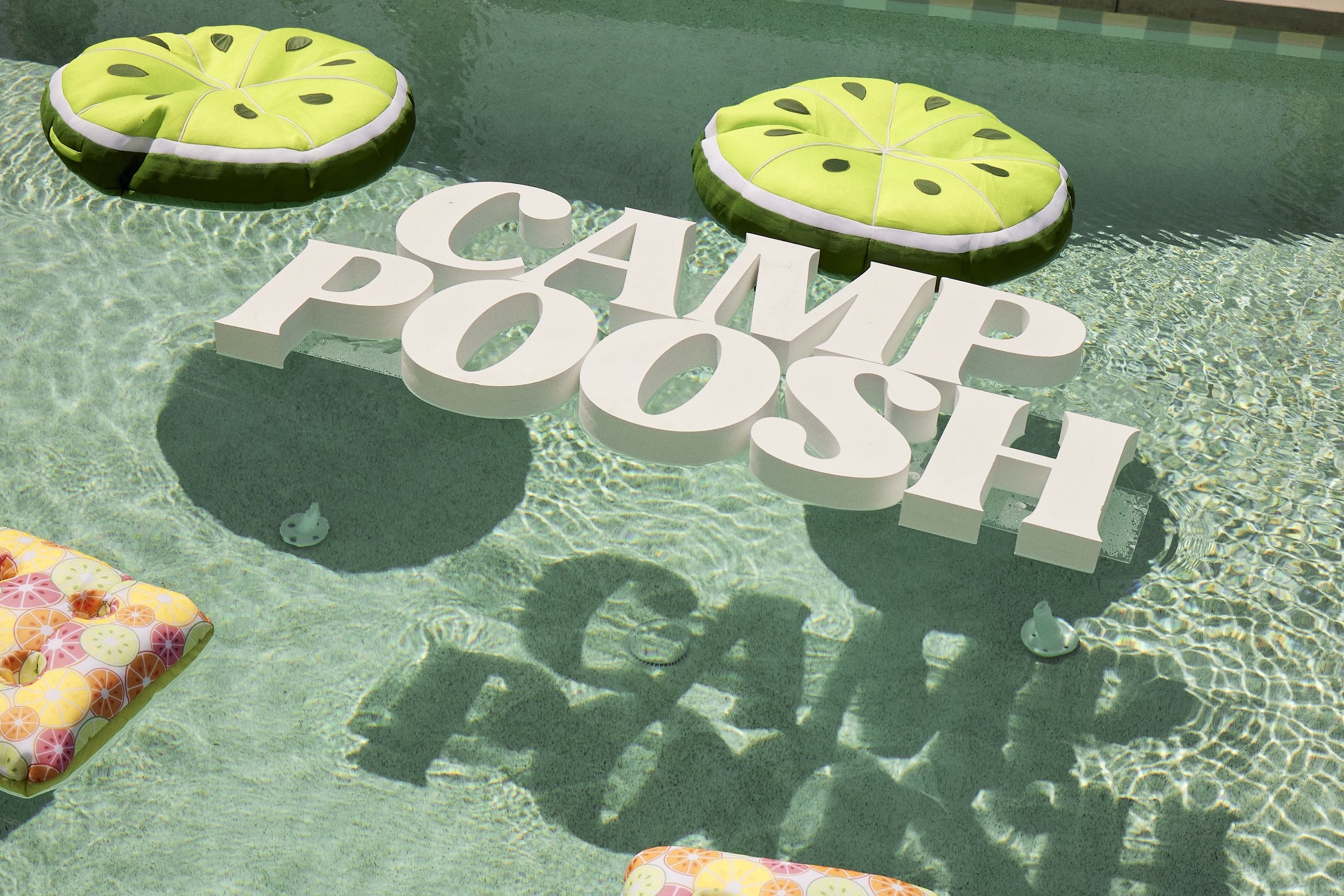 white Camp Poosh sign floating in pool
