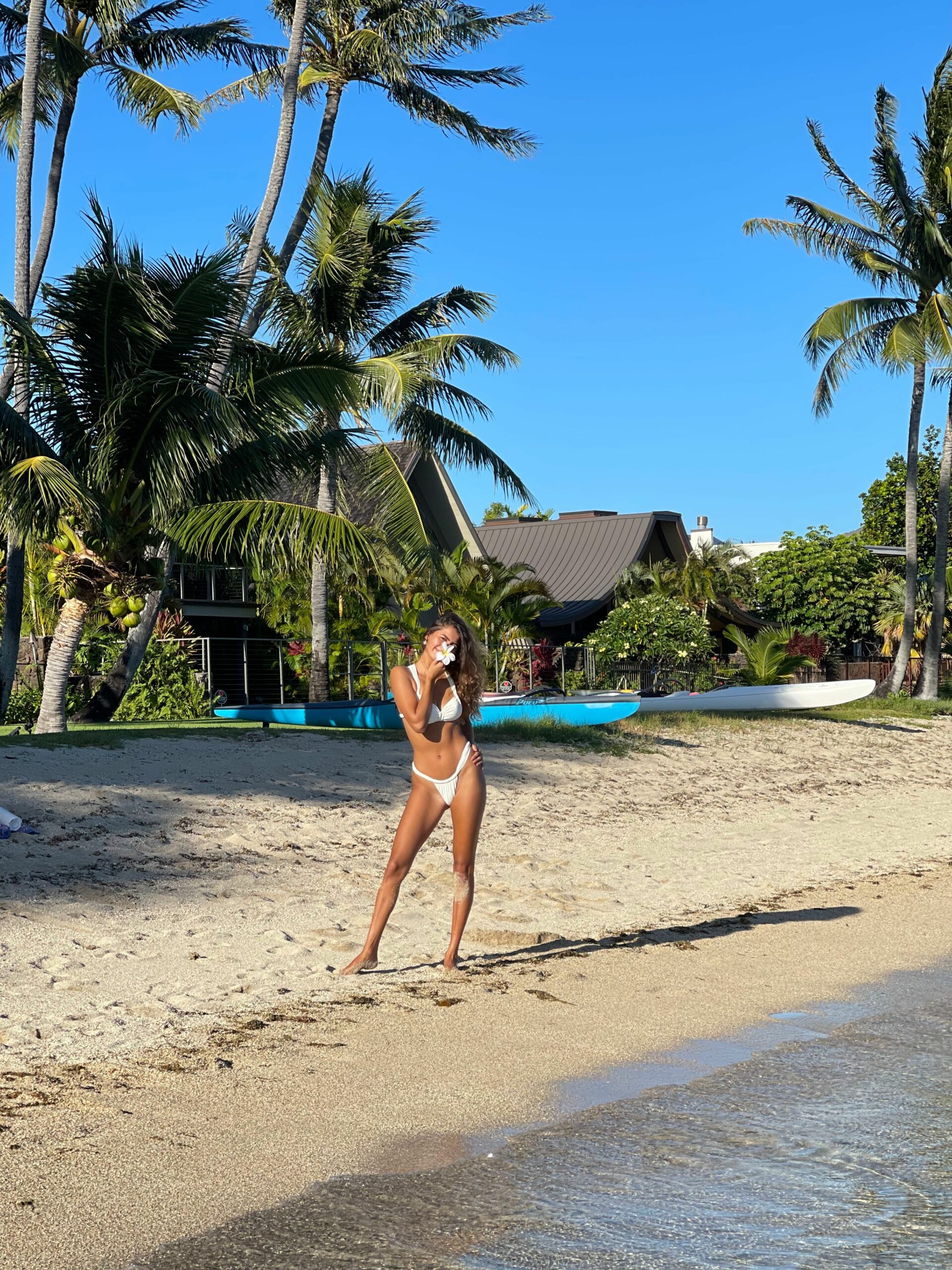 woman posing on tropical beach smelling a flower